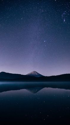 the night sky with stars above a mountain and lake in front of it is reflected in water