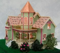 a doll house is shown on top of a fake grass field with flowers and bushes