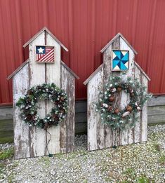 two wooden barns with wreaths and decorations on the doors are sitting in front of a red wall