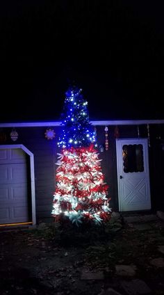 a red white and blue christmas tree in front of a house with lights on it