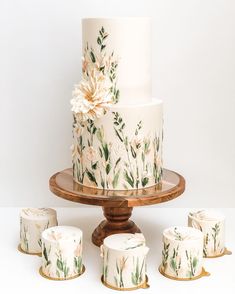 there is a white cake with flowers on it and six smaller cakes next to it