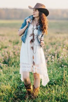 a woman in a white dress and cowboy hat is standing in a field with flowers