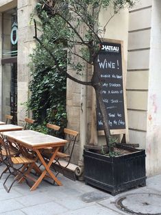 an outdoor cafe with tables and chairs on the sidewalk next to a sign that says wine