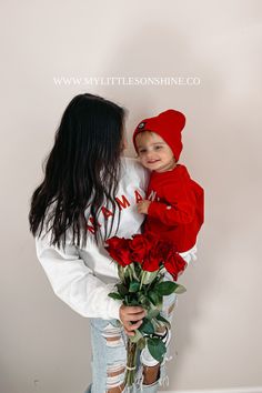 a woman holding a baby in her arms with red roses on the bottom of her chest