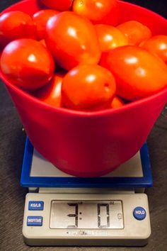 a red bowl filled with tomatoes on top of a scale