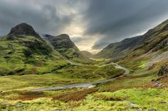 a road winding through the mountains with green grass on both sides and dark clouds in the sky