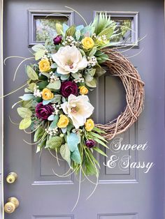 a wreath on the front door with flowers and greenery hanging from it's side