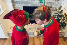 two young children dressed in red and green clothing standing next to each other near a fireplace