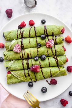 a white plate topped with green crepes covered in chocolate and raspberries