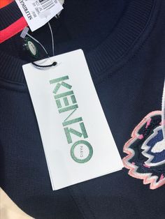 a tag is attached to a sweater that says kenko on it and sits next to other clothing items