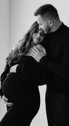 a pregnant couple cuddles in black and white