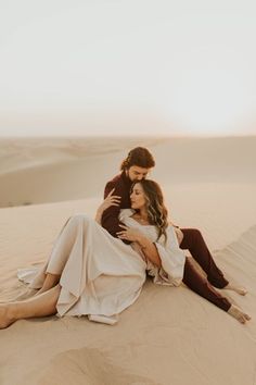 a man and woman sitting on top of a sand dune