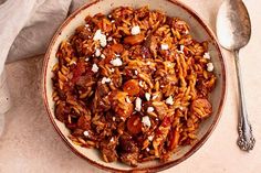 a bowl filled with pasta and meat on top of a table next to a spoon