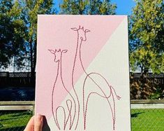 a person holding up a pink and white painting with two giraffes on it