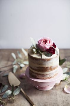 a three tiered cake sitting on top of a wooden table next to pink flowers