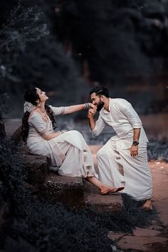 two people are sitting on the ground in front of a waterfall and one person is touching another's hand