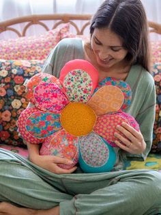 a woman sitting on a bed holding a bunch of pillows and a flower shaped pillow