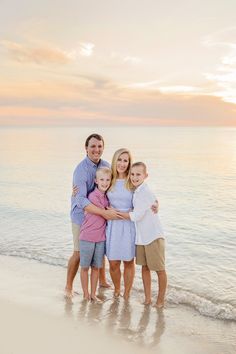 a family standing on the beach at sunset with their arms around each other and smiling