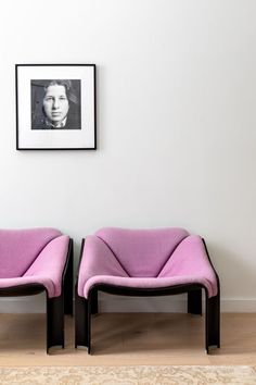 two pink chairs sitting next to each other in front of a framed photo on the wall