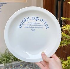 a person holding up a white plate with words on it that reads books cup of tea