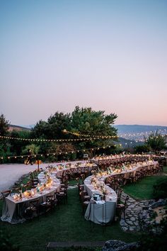 an outdoor dinner is set up with long tables and lights strung from the trees above