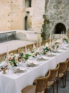 a long table with white plates and flowers on it in front of an old building