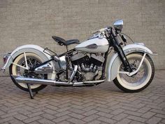 a white motorcycle parked on top of a brick road next to a wall and sidewalk