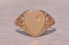 This stunning piece, known as The Classic Heart, features a beautifully engraved heart signet with a natural diamond accent. The ring is crafted in yellow gold, showcasing intricate filigree work on the shank that adds a touch of elegance. The ring is currently a finger size 6 but can be adjusted to any finger size for an additional charge upon request, ensuring a perfect fit. Love this piece, but don't have the money to spend right now? We offer FREE layaway on every item in our shop. With just 20% down, take one full year (interest-free) to pay off your new jewelry! There are no hidden fees or charges, ever. For more information on our layaway policy, please contact us. Each piece has been hand-selected and meticulously identified and graded by a Graduate Gemologist who has been awarded Signet Rings, Yellow Gold Ring, The Money, Signet Ring, Yellow Gold Rings, Rings Statement, Gold Ring, Statement Rings, Natural Diamonds