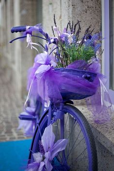 a purple bicycle with flowers tied to the handlebars is parked next to a window