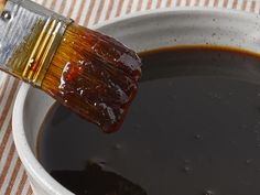 a paintbrush is being dipped with brown liquid in a white bowl on a striped tablecloth