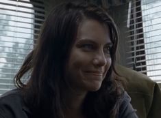 a woman sitting in front of a window with blinds