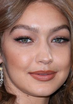 a close up of a woman with blue eyes and brown hair, wearing large earrings