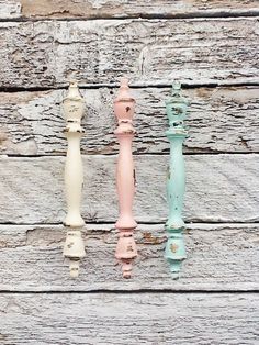 three different colored candles sitting on top of a wooden table next to an old wall