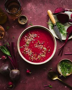 a bowl of beet soup with garnishes and herbs on the side