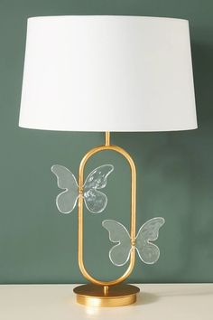 a lamp that is on top of a table with a white shade and some butterflies