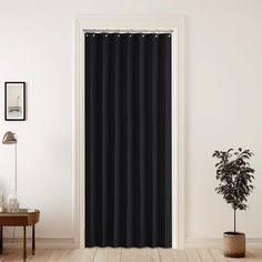 a black curtain hanging on the side of a white wall next to a potted plant