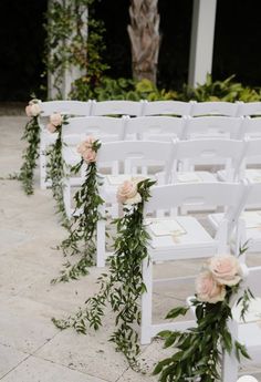 rows of white chairs decorated with flowers and greenery