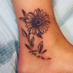 a sunflower tattoo on the foot with words written in cursive writing below it