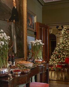 a dining room table covered in food and vases filled with flowers next to a christmas tree