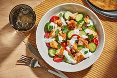 a white plate topped with cucumbers and tomatoes next to a bowl of pita bread