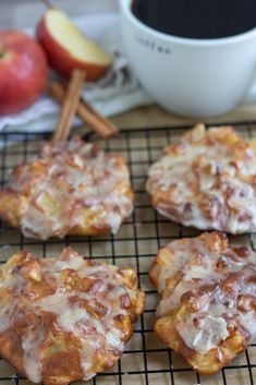 four cookies on a cooling rack with apples and cinnamon sticks in the background, next to a cup of coffee