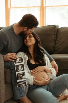 a man and woman cuddle on the couch as they hold their baby bump up