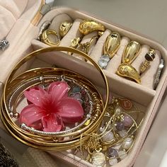 a pink flower sitting inside of a box filled with gold rings and other jewelry items