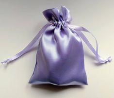 a purple satin bag with a bow on the front and side, sitting on a white surface