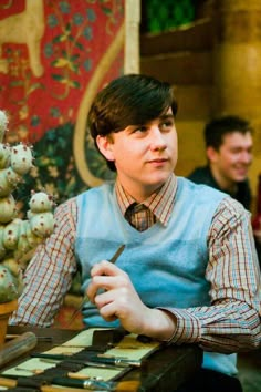 a young man sitting at a table in front of a christmas tree holding a pair of scissors