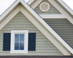 the top of a gray house with blue shutters and a clock on it's face