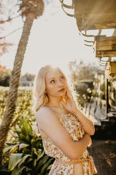 a woman standing in front of some trees and palm trees with her hand on her ear