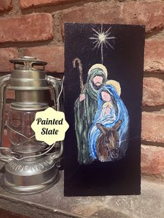 a christmas card with an image of the nativity scene painted on it next to a lantern