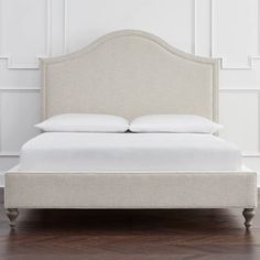 an upholstered bed with white sheets and pillows