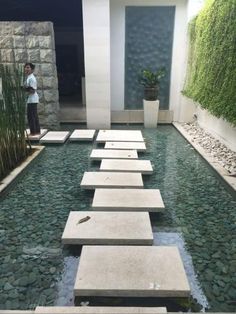 a man standing in front of a pool with stepping stones on the water and plants